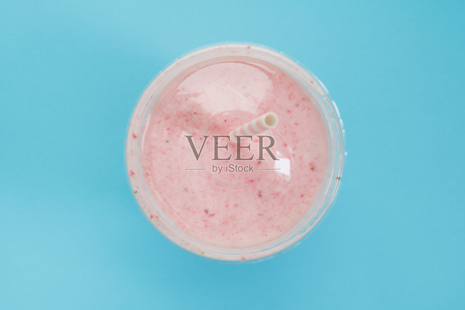 俯视图草莓奶昔在一个塑料杯与吸管在一个蓝色的背景。柔和的颜色。夏日健康生活理念。照片摄影图片