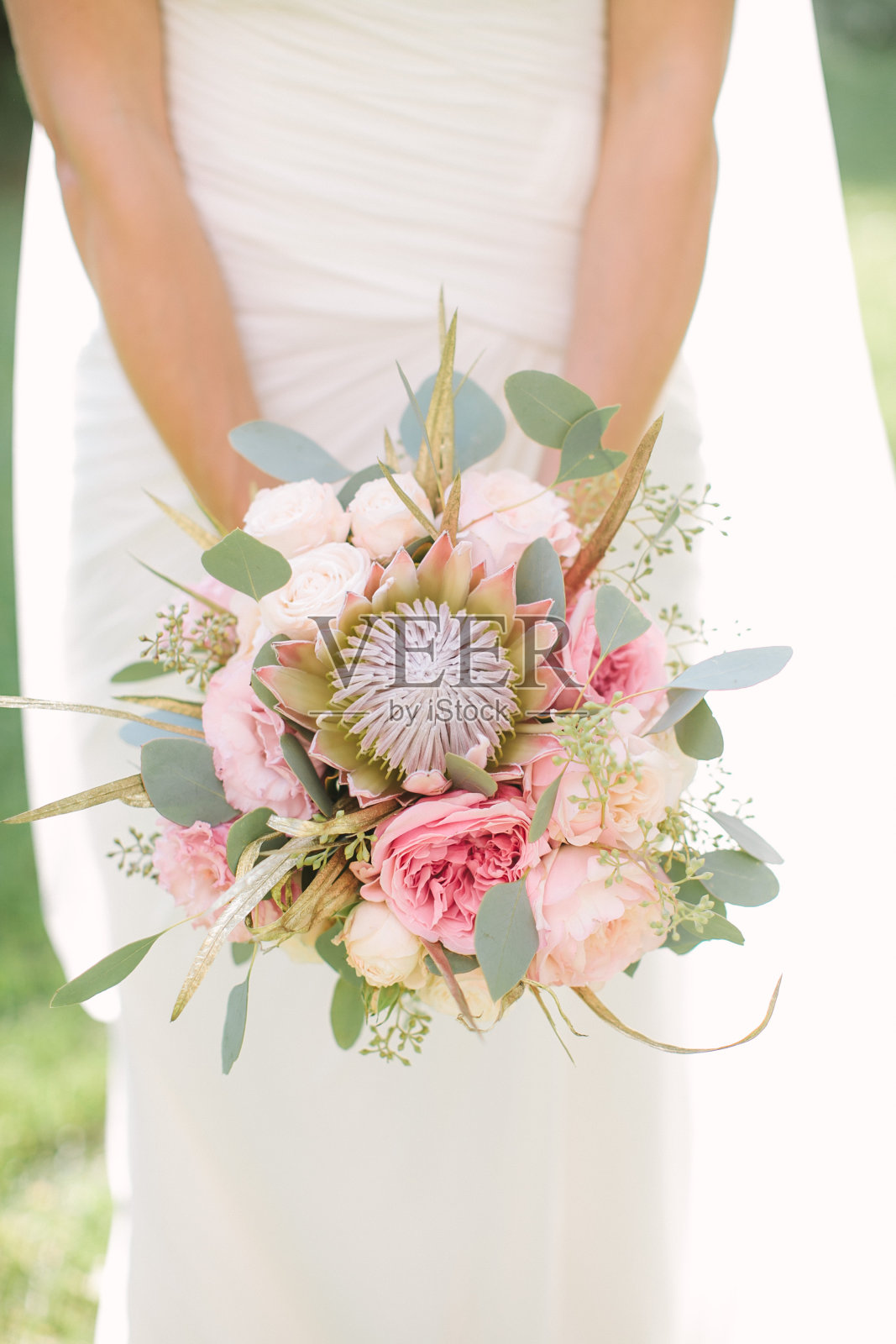 优雅的新娘身穿白色婚纱，手拿一束粉红色玫瑰、牡丹和桉树制成的婚礼花束照片摄影图片