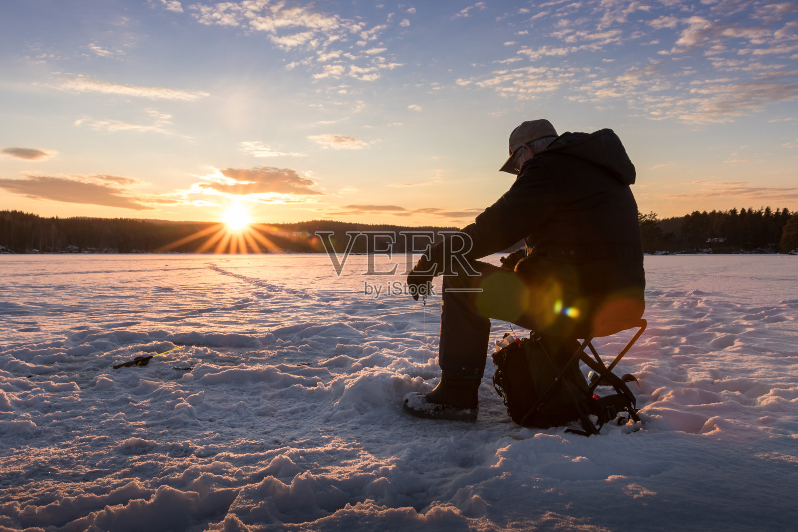 日落时在挪威的一个湖上冰上钓鱼。照片摄影图片