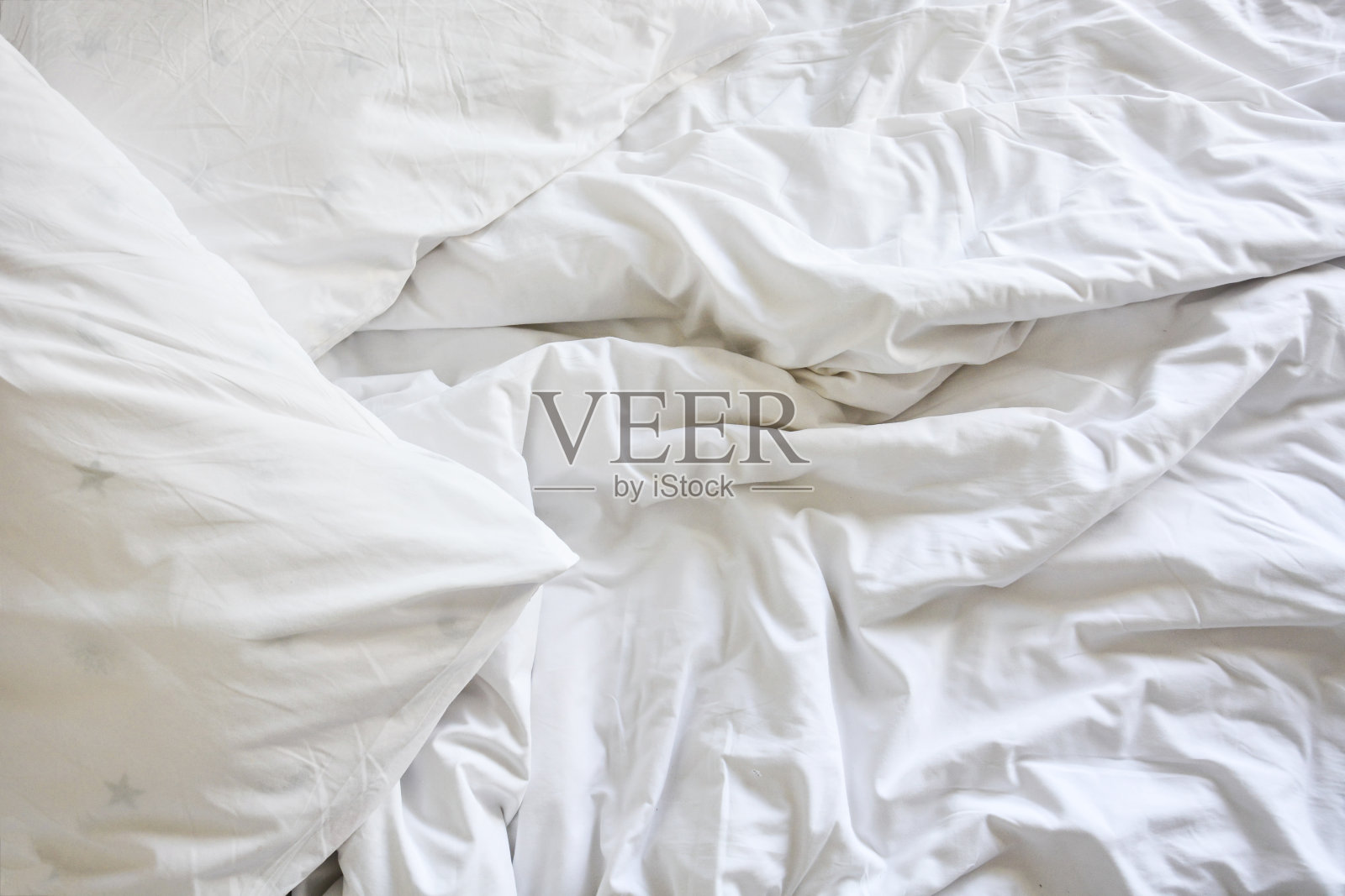 在床上放着白色的枕头和皱褶凌乱的毯子，早上醒来后躺在卧室里，睡了一个漫长的夜晚。照片摄影图片
