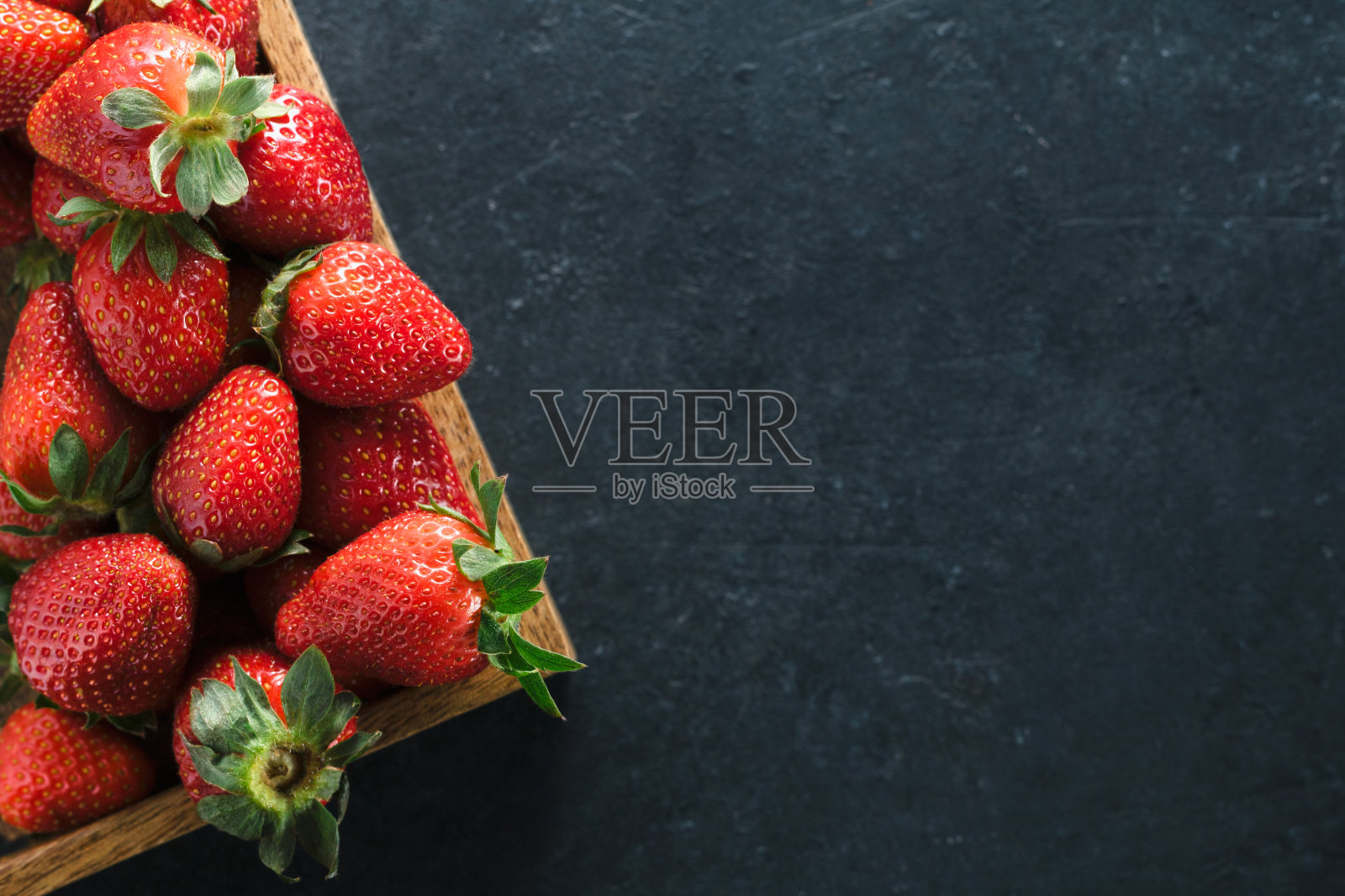 俯视图的一个木制的盒子与成熟的新鲜草莓在一个黑色的桌子上。放置文本。健康食品的概念。照片摄影图片