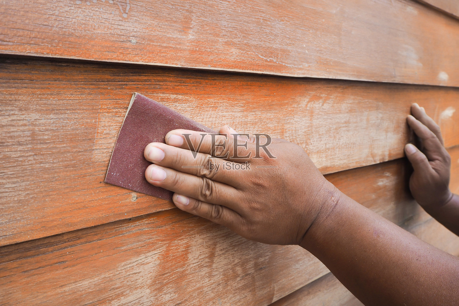 人的双手用砂纸擦洗木墙。照片摄影图片