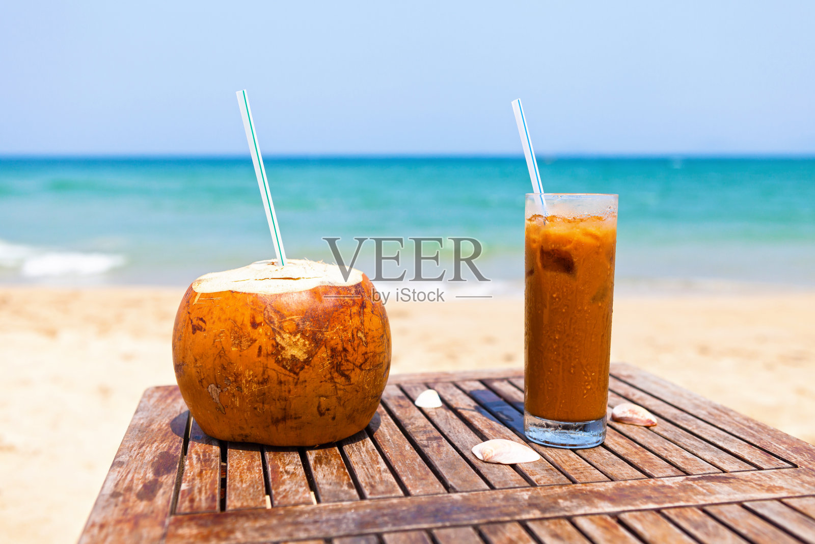 木桌上放着椰汁和冰咖啡，背靠美丽的海滩和翠绿的大海照片摄影图片