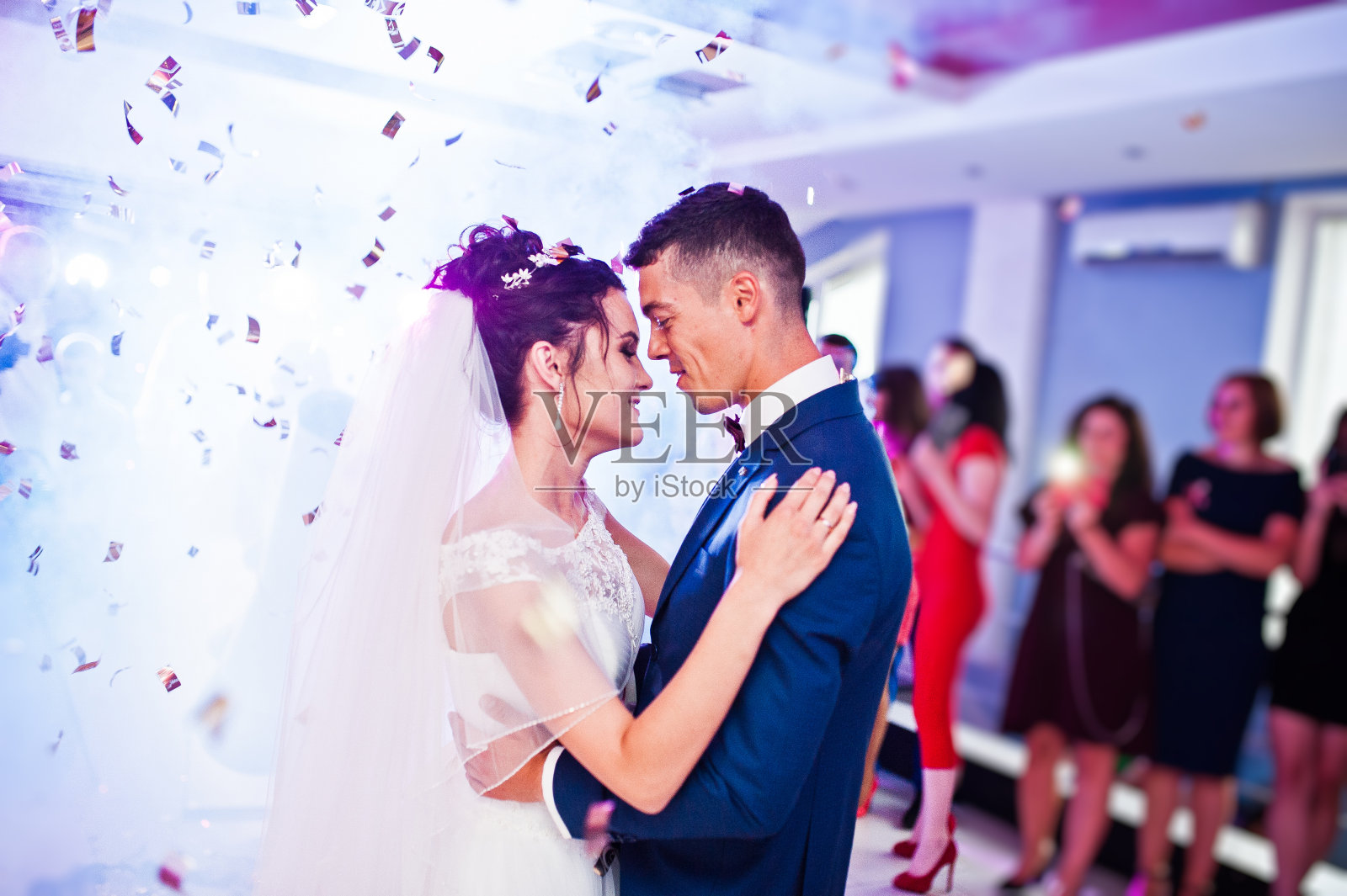 这是新人在婚礼上以五彩纸屑和彩灯为背景的感人的第一支舞。照片摄影图片