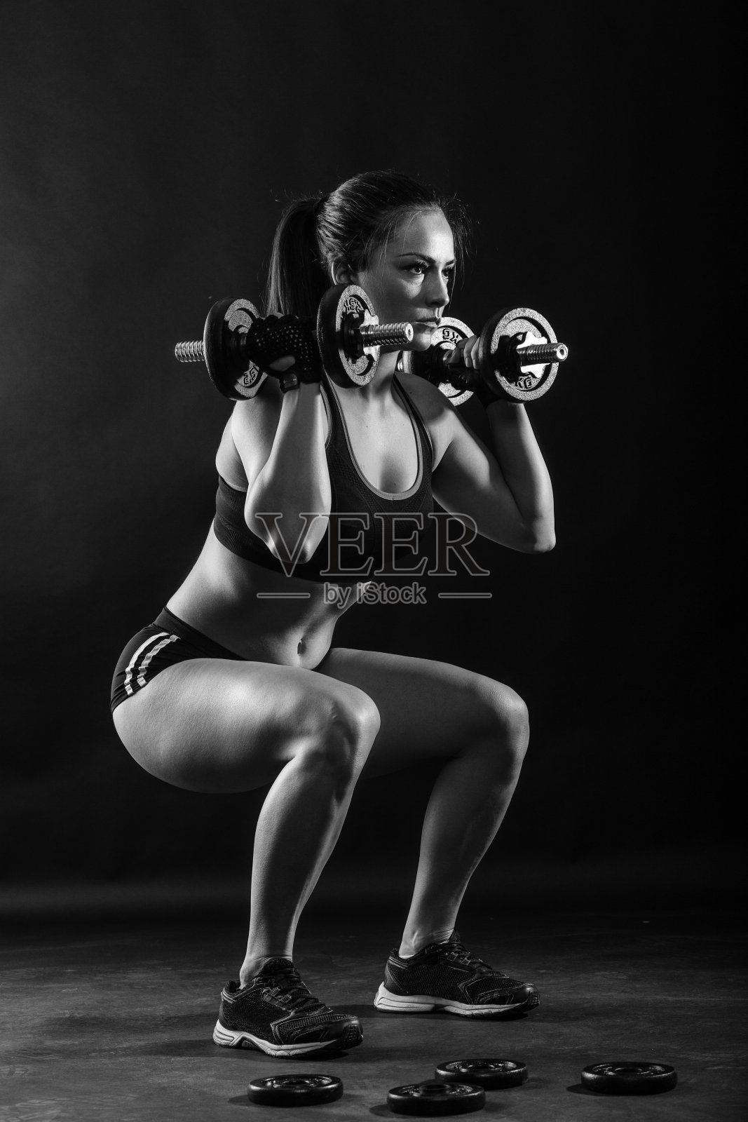 女性健美运动员举着哑铃孤立在黑色背景，黑色和白色。照片摄影图片