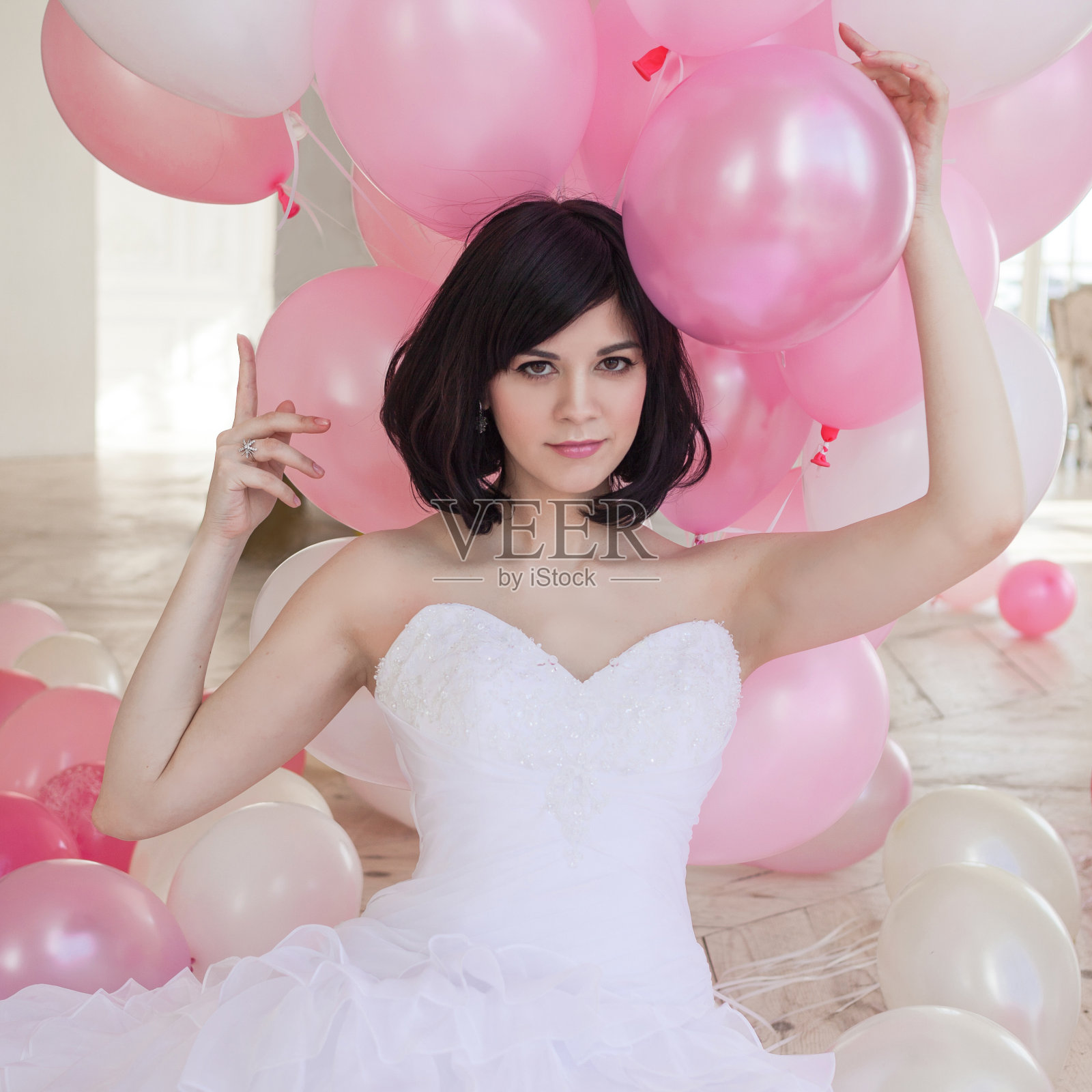 穿着婚纱的年轻女子在奢华的室内装饰着一堆粉色和白色的气球。照片摄影图片