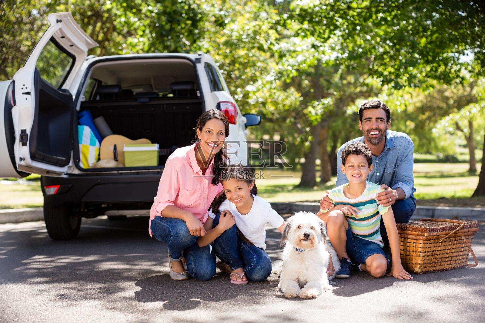 快乐的一家人坐在他们的车旁边野餐照片摄影图片