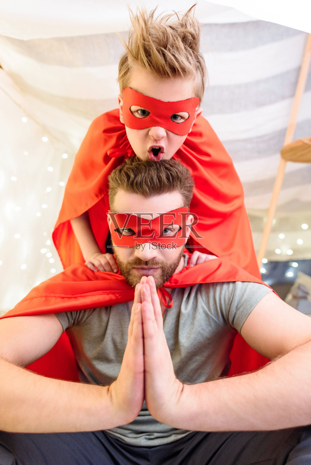 父亲和儿子穿着超级英雄的服装在毯子堡一起玩照片摄影图片