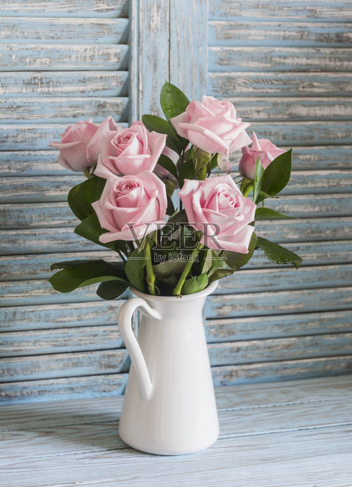 白色搪瓷壶上的粉色玫瑰，以乡村的木制背景为背景照片摄影图片