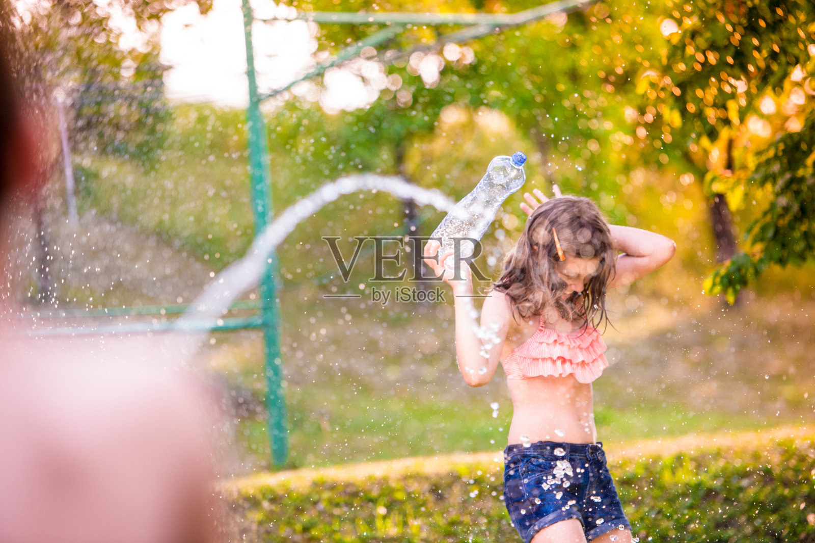 一个面目全非的男孩用水枪向女孩泼水，阳光明媚的夏天照片摄影图片