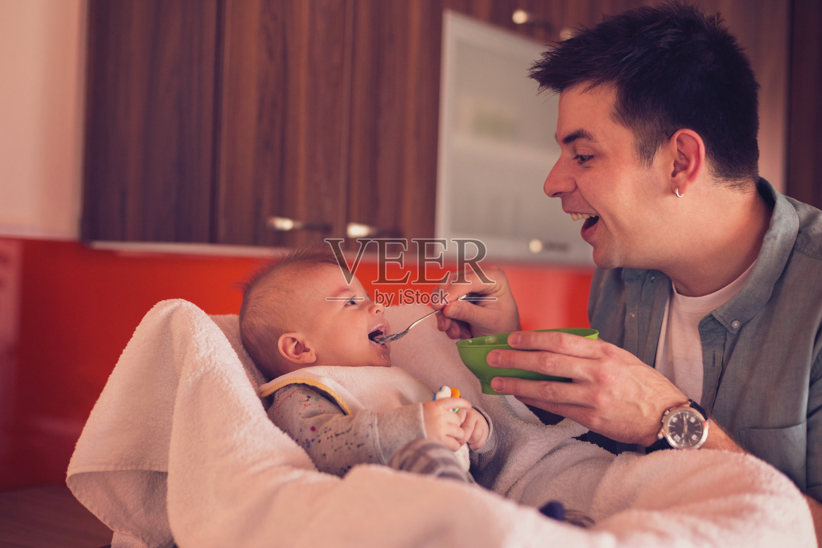 年轻的单身父亲正在喂养一个漂亮的男婴照片摄影图片