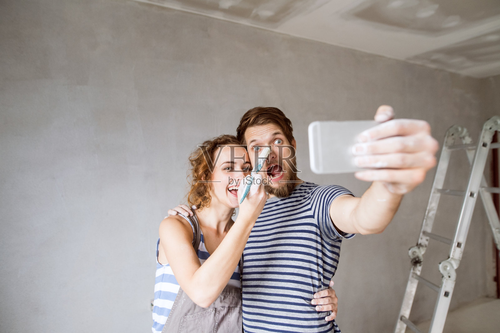 夫妇在家里刷墙，用智能手机自拍。照片摄影图片
