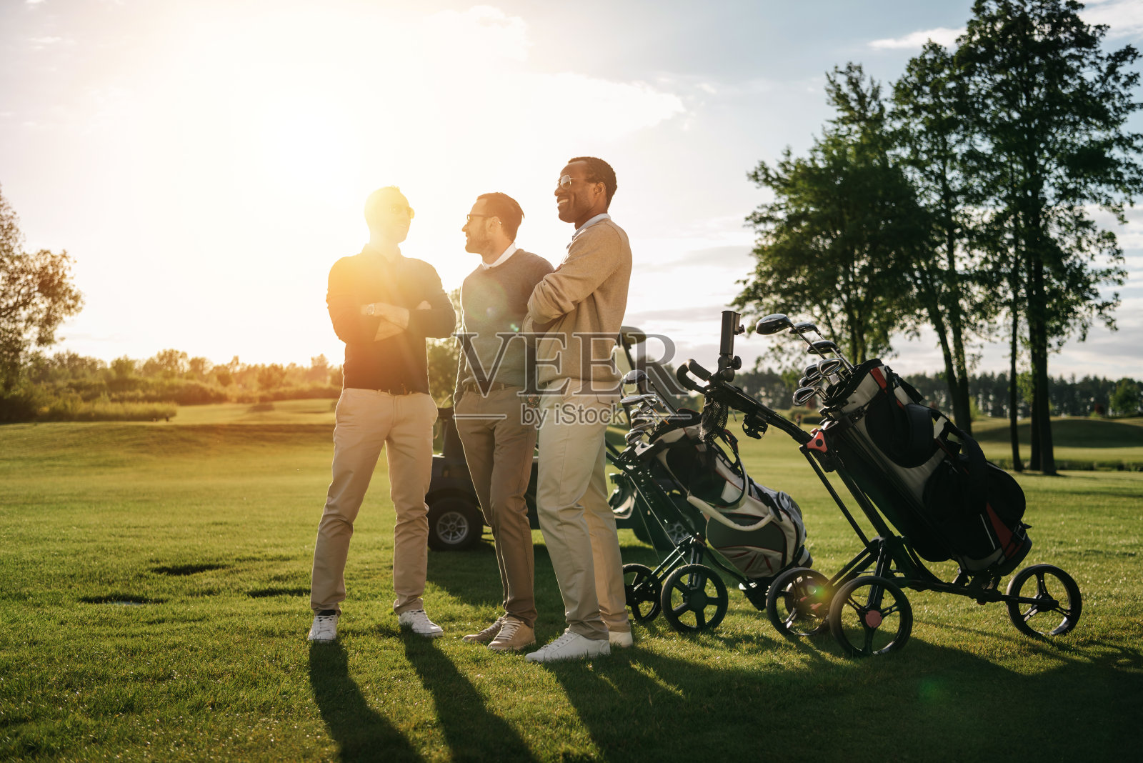 三个面带微笑的男人双手交叉站在装在袋子里的高尔夫球杆旁照片摄影图片