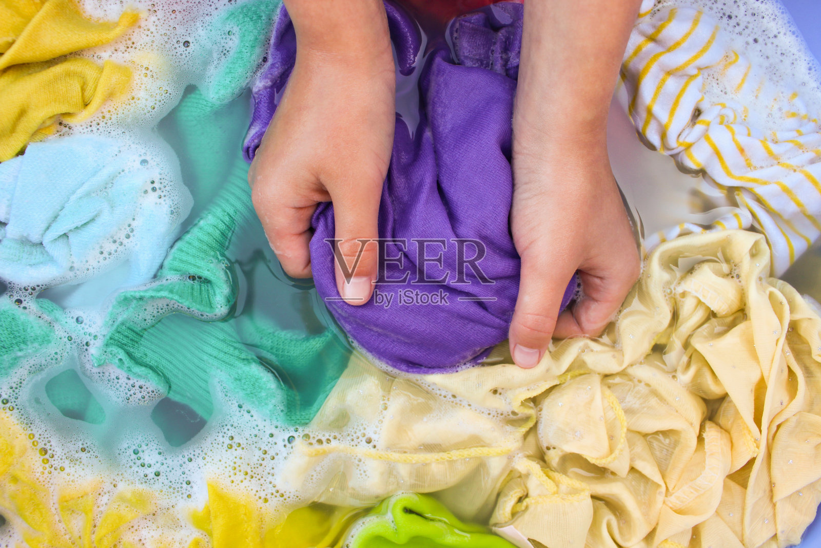 女性用手在盆里洗彩色衣服。照片摄影图片