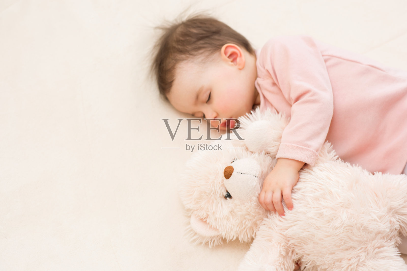 近距离拍摄的美丽的婴儿蹒跚学步的女孩和一个毛茸茸的泰迪熊在床上睡觉照片摄影图片