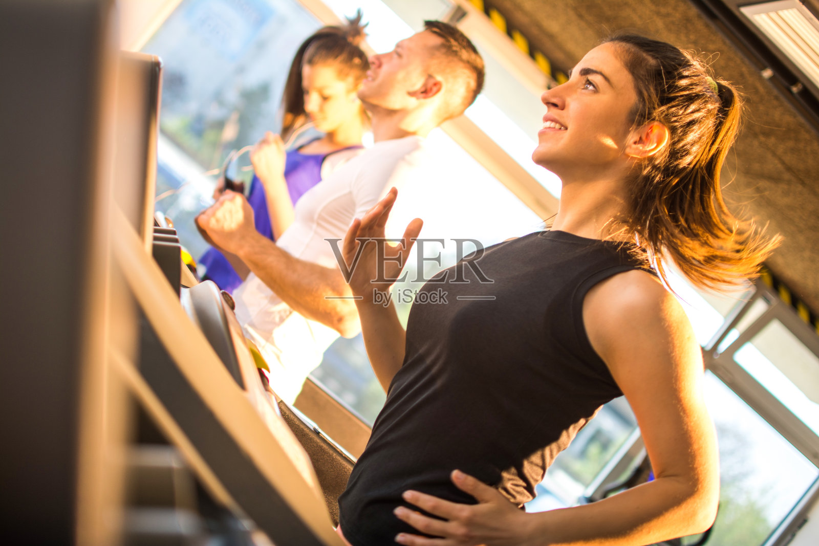 爱运动的年轻女子在健身房里的跑步机上跑步。照片摄影图片