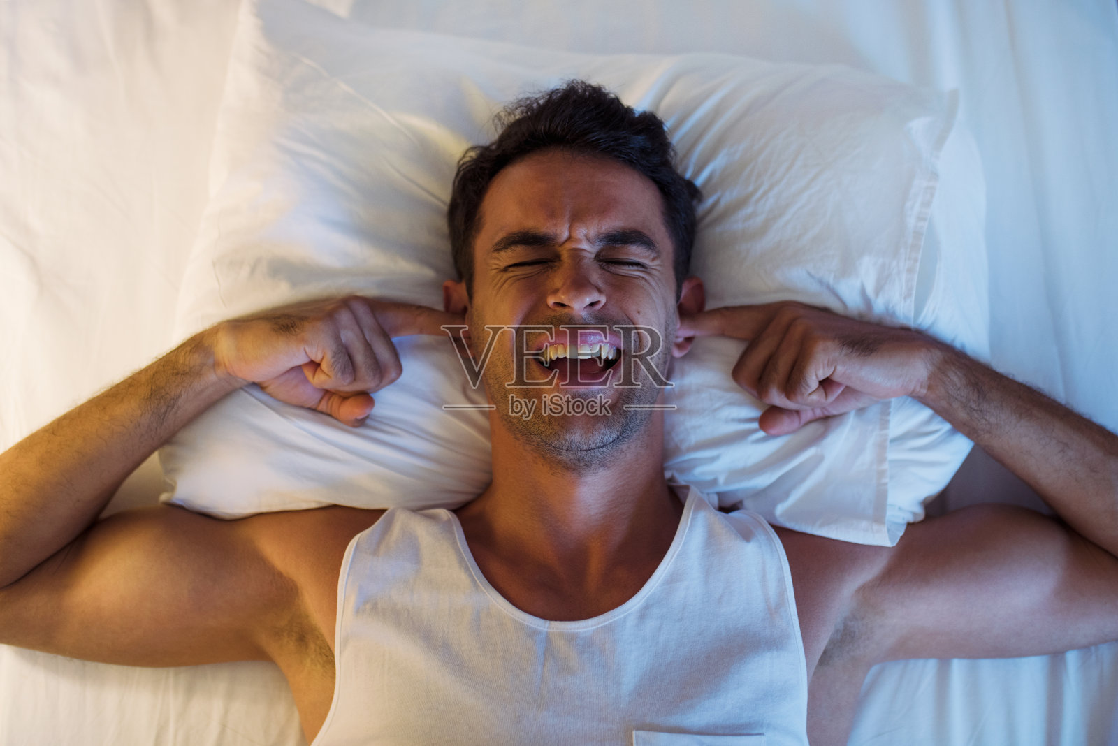 英俊的微笑的年轻人在白色的床上使用手机和短信。在卧室背景照片摄影图片