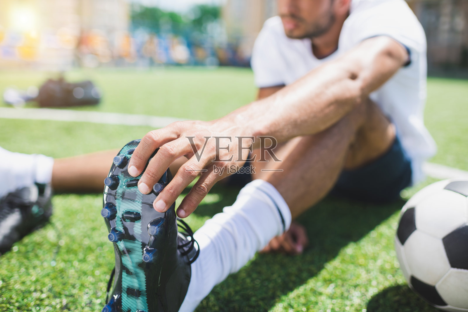 选择焦点的足球运动员持有足球靴，而坐在球场上照片摄影图片