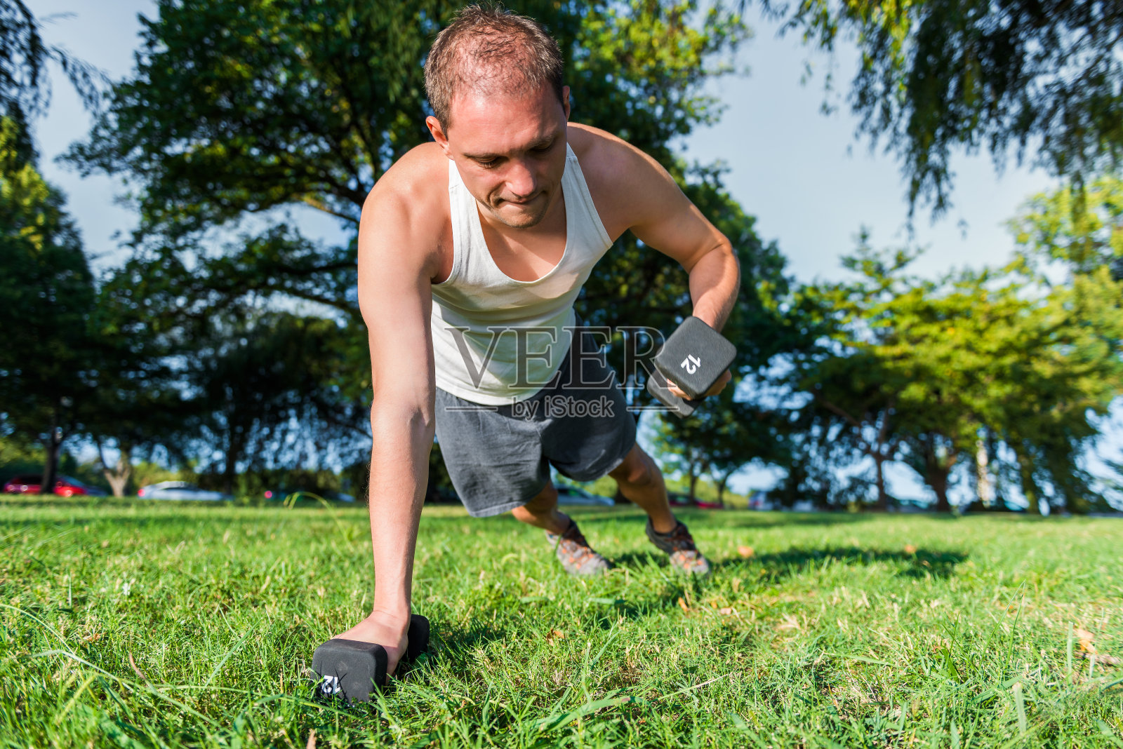 一个年轻健康男子在草地上举哑铃的特写照片摄影图片