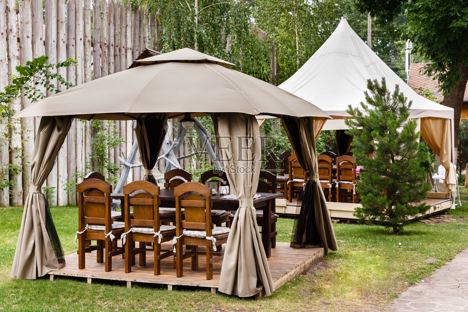 两个带有木制桌椅的帆布帐篷。森林餐厅的复古设计照片摄影图片