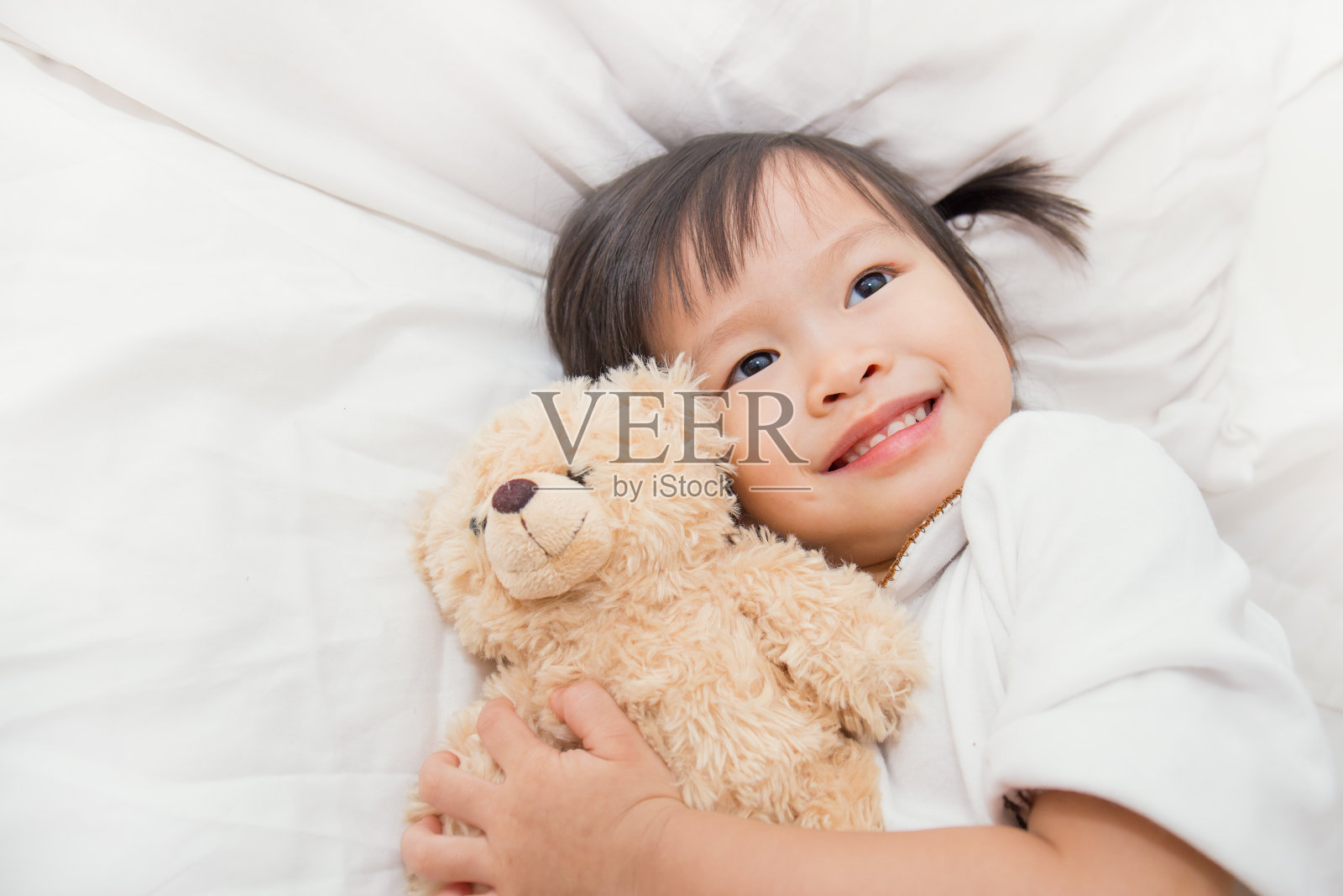 亚洲可爱的小女孩拥抱泰迪熊在床上照片摄影图片