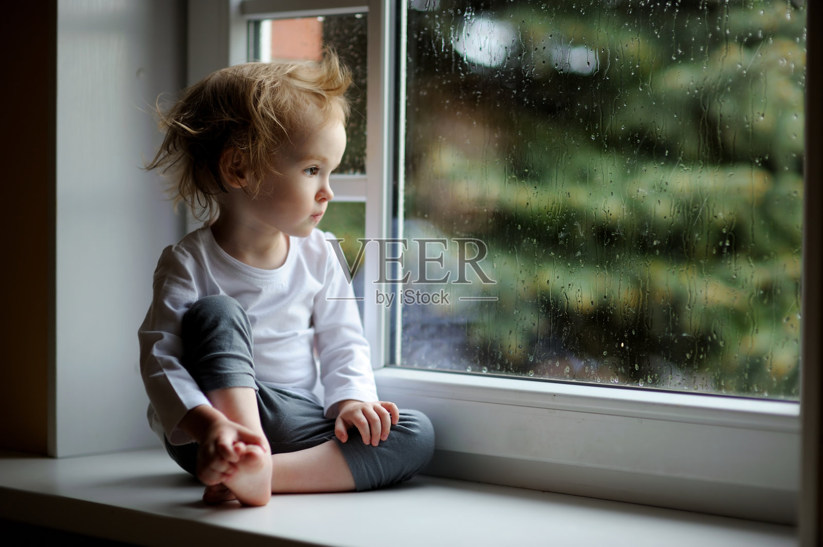 可爱的蹒跚学步的小女孩望着窗外照片摄影图片