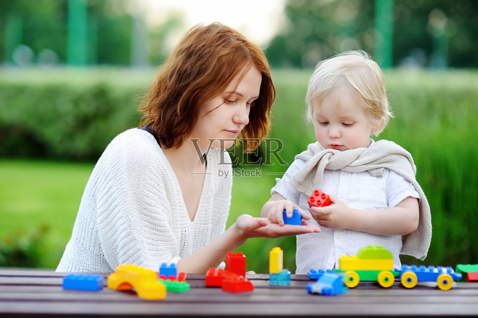 一个年轻的女人和他蹒跚学步的儿子在玩五颜六色的塑料积木照片摄影图片