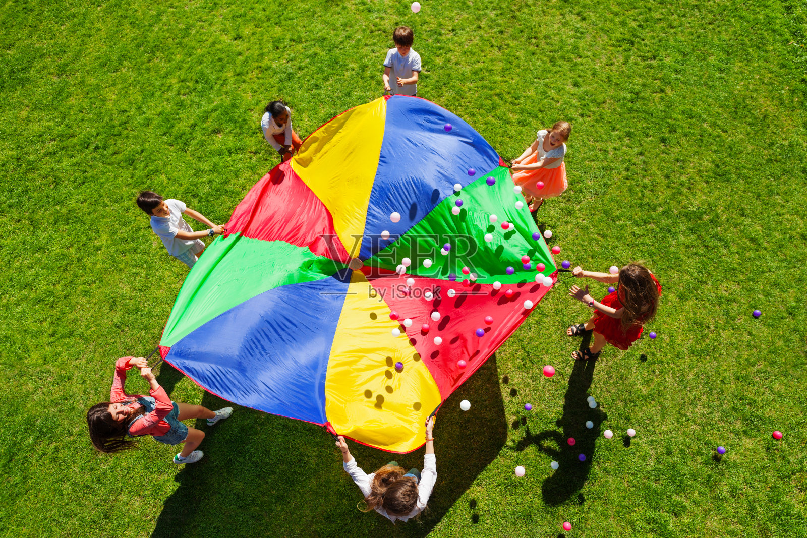 快乐的孩子们挥舞着装满彩球的彩虹降落伞照片摄影图片