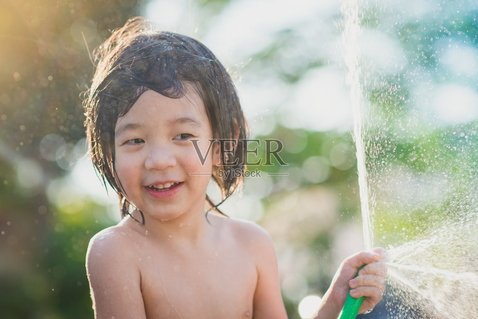 可爱的亚洲男孩玩水从软管户外照片摄影图片
