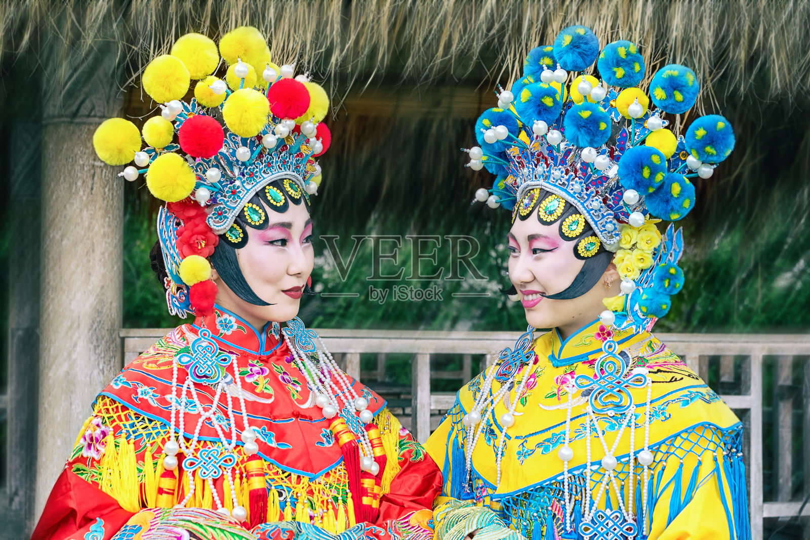 两个美丽的中国女孩的肖像，穿着传统的中国服装，戴着帽子和绒球看着对方照片摄影图片