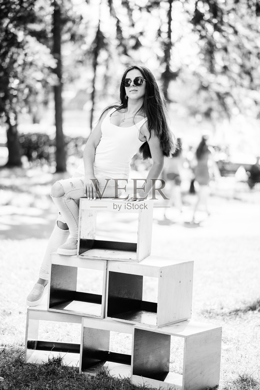 一个阳光明媚的日子里，一个穿着时尚的女孩在公园的木箱上摆姿势。黑白照片。照片摄影图片