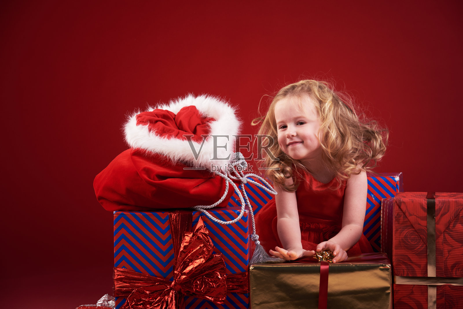 红色背景上有圣诞礼物的可爱小女孩。照片摄影图片