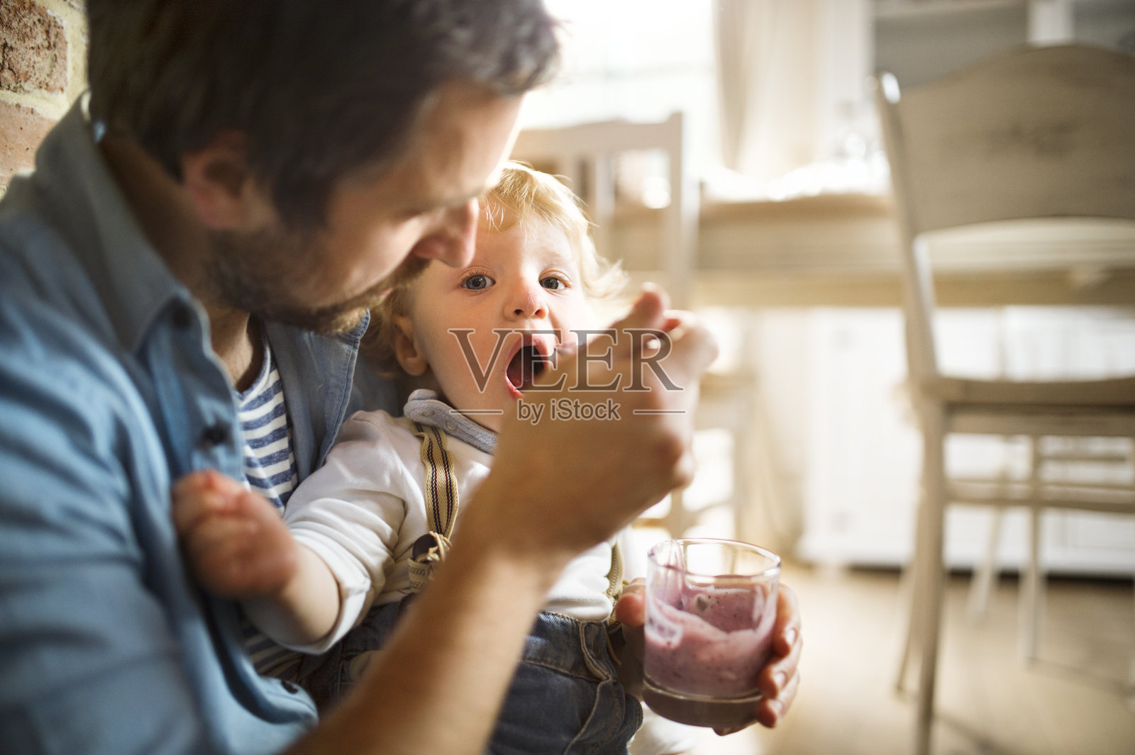 年轻的父亲在家里用酸奶喂他的小儿子。照片摄影图片
