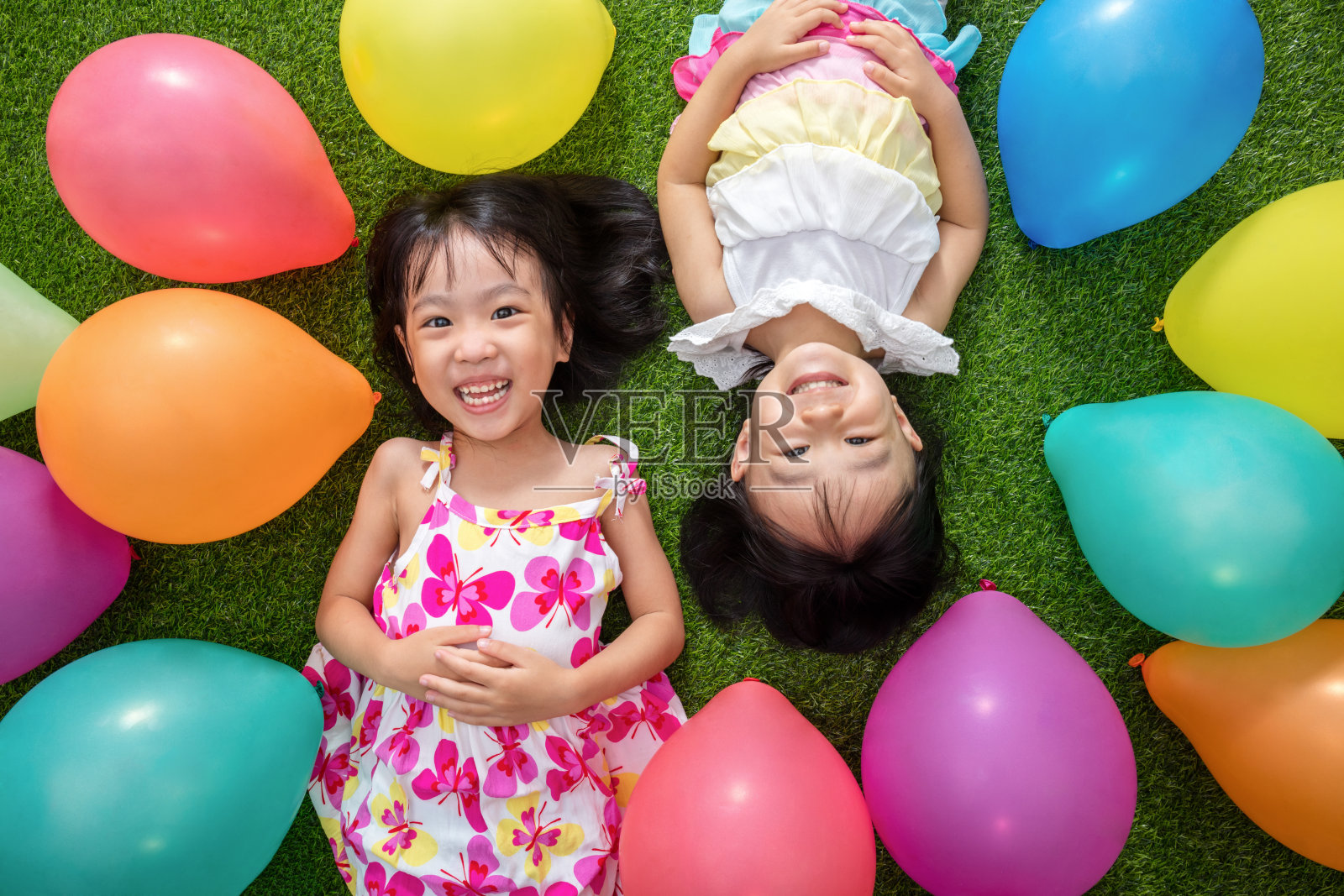 亚洲的中国小女孩们躺在草地上，中间是彩色的气球照片摄影图片