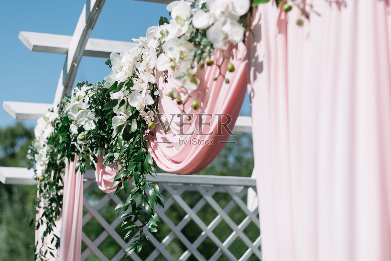 夏季户外婚礼的漂亮装饰。婚礼拱门由轻布和白色和粉红色的花朵在绿色的自然背景。白色木门，乡村风格照片摄影图片