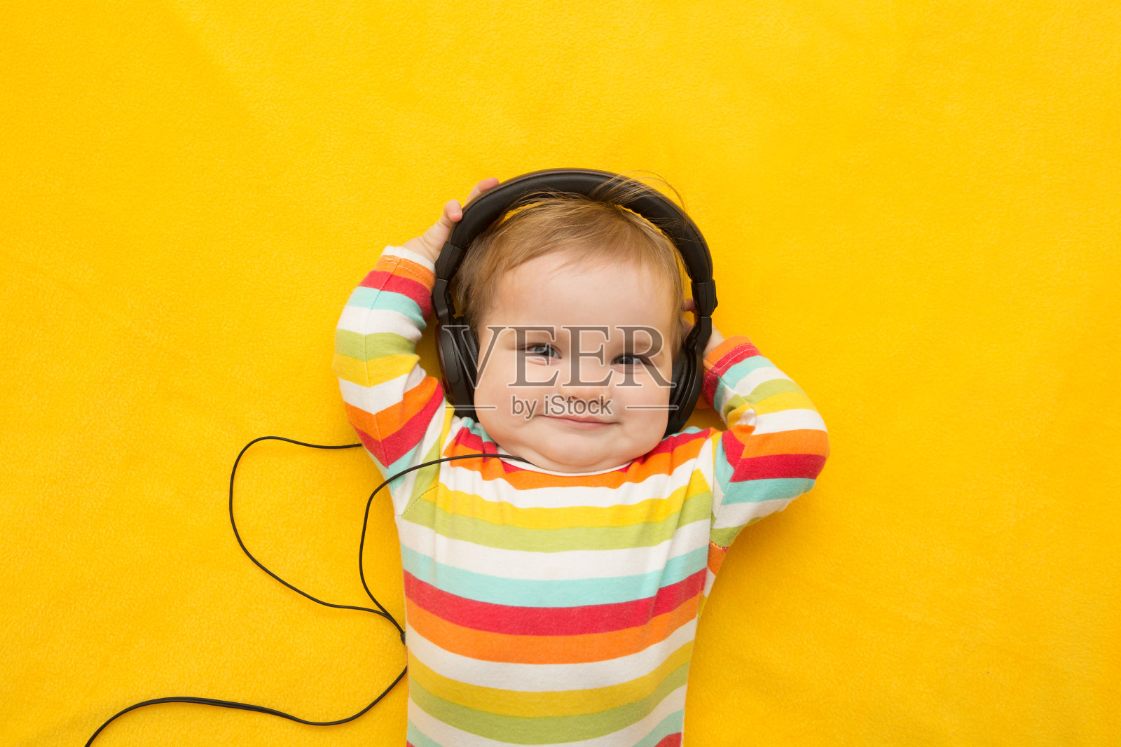 黄色背景上戴着耳机的婴儿照片摄影图片