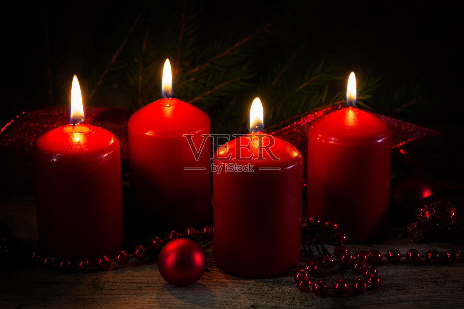 在第四个降临节，四支燃烧着的红色蜡烛，用云杉树枝和小装饰品装饰在乡村木板上，黑色的背景照片摄影图片