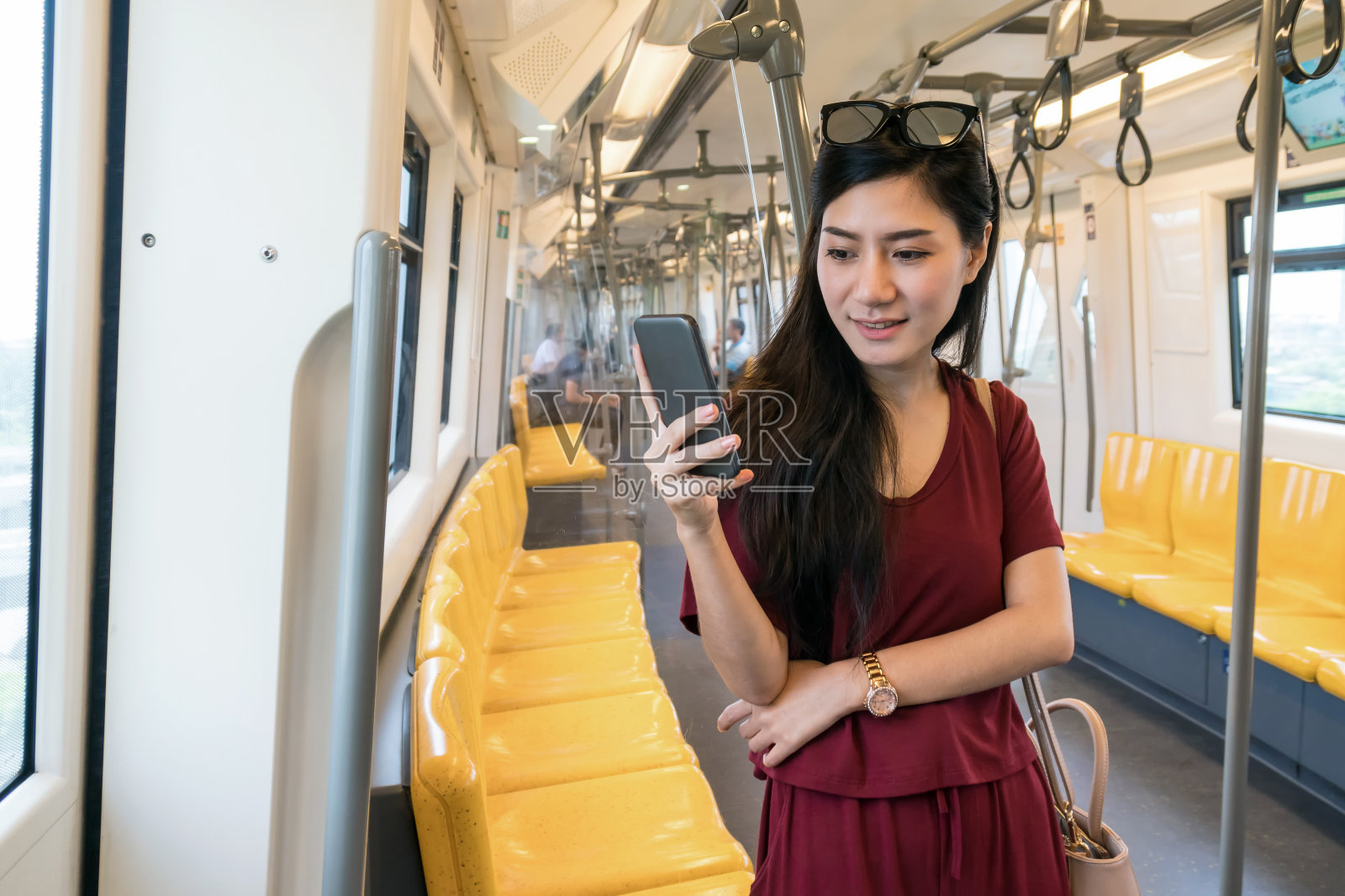 亚洲女性乘客休闲套装通过智能手机在Skytrain轨道或地铁上使用社交网络，在大城市旅行，生活方式和交通理念照片摄影图片