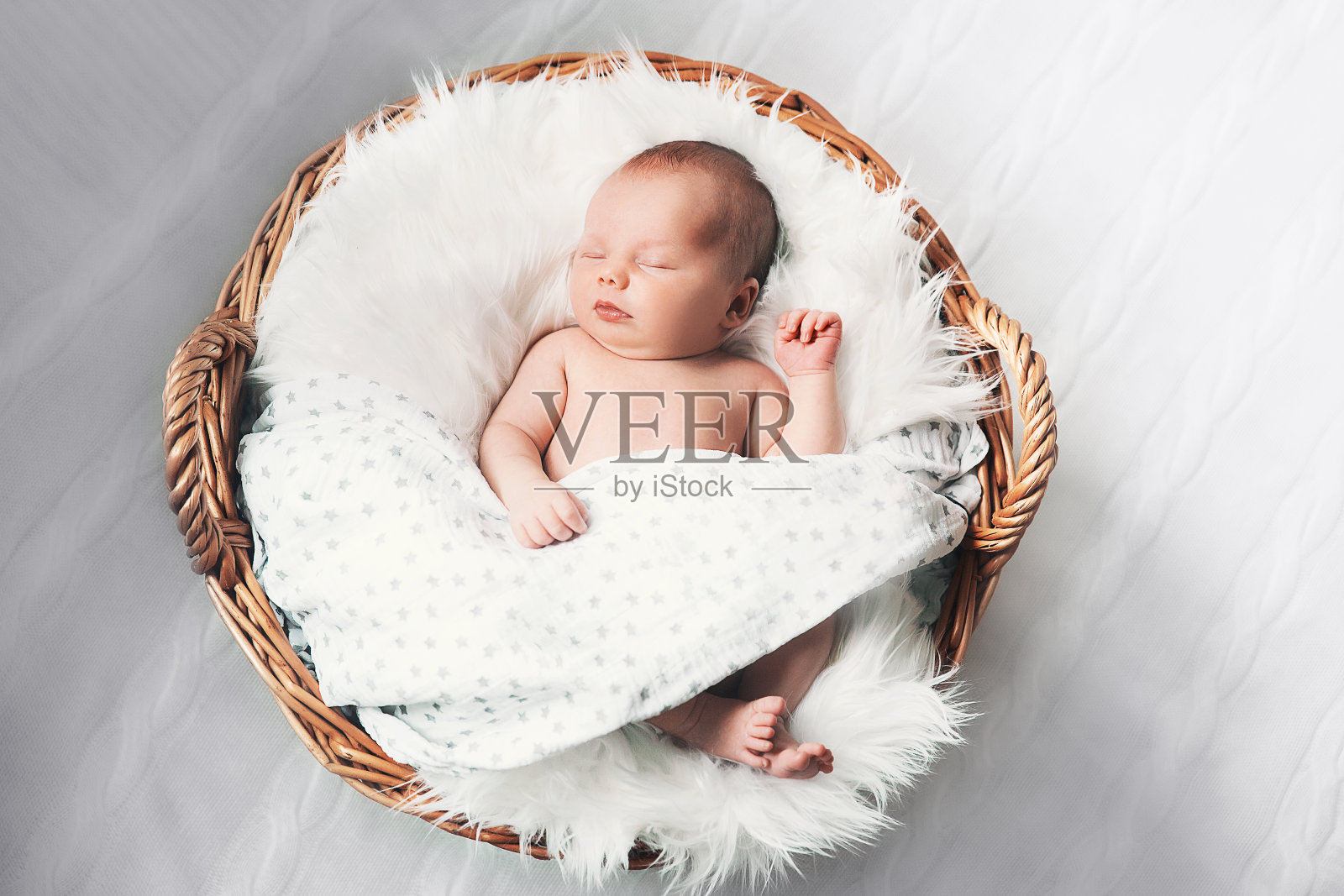 熟睡的新生婴儿躺在柳条篮子里的白毯子上。照片摄影图片