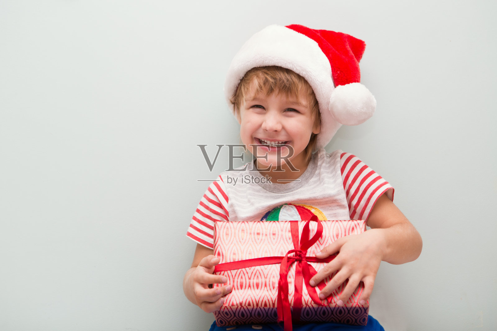 快乐的孩子戴着圣诞老人的红帽，拿着圣诞礼物。圣诞节的时间。照片摄影图片
