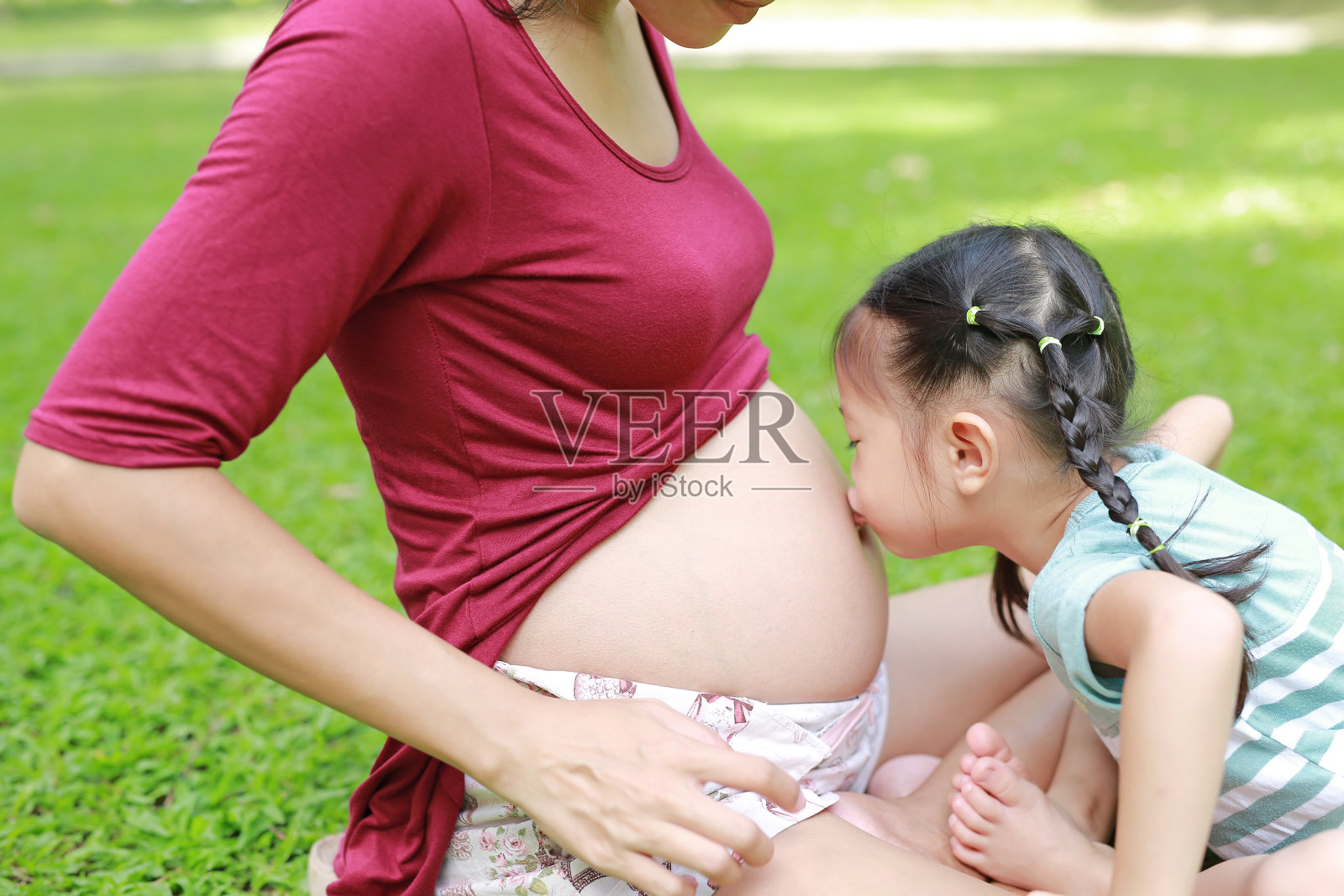 快乐的孩子在花园里亲吻孕妇的肚子。照片摄影图片