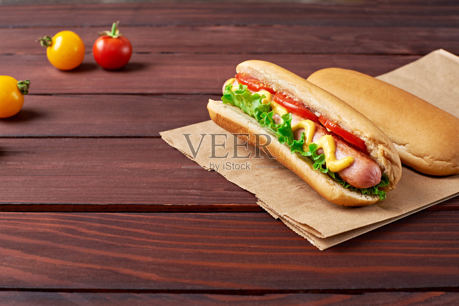 两个美味的热狗在手工纸袋，香肠和西红柿在木制背景。照片摄影图片