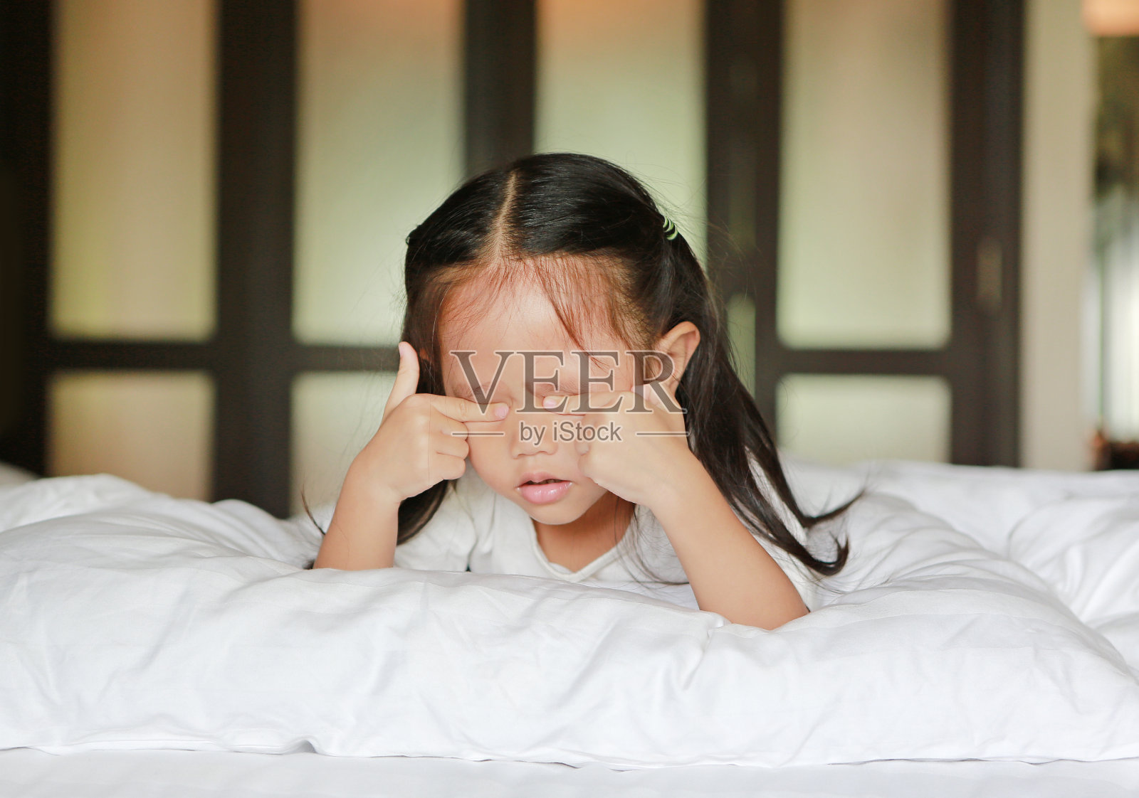 可爱的亚洲小女孩躺在床上揉眼睛。照片摄影图片