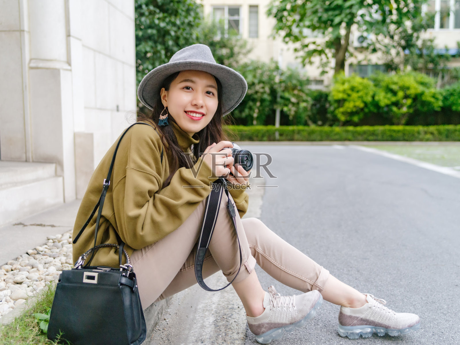 美丽的中国女人坐在路边，微笑着拿着相机，旅行的概念。照片摄影图片