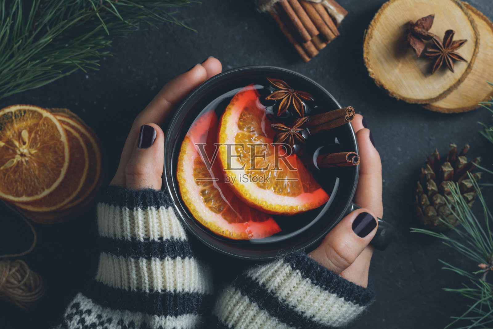 俯视图的女孩的手在一个冬天的毛衣是拿着一个大的黑色杯热热的热葡萄酒。舒适的冬季假期的概念。照片摄影图片