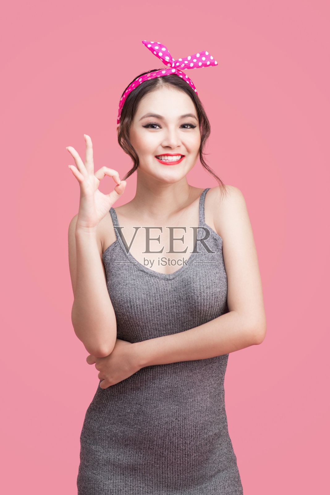 亚洲女孩的肖像与漂亮的微笑在海报风格与手势在粉红色的背景照片摄影图片