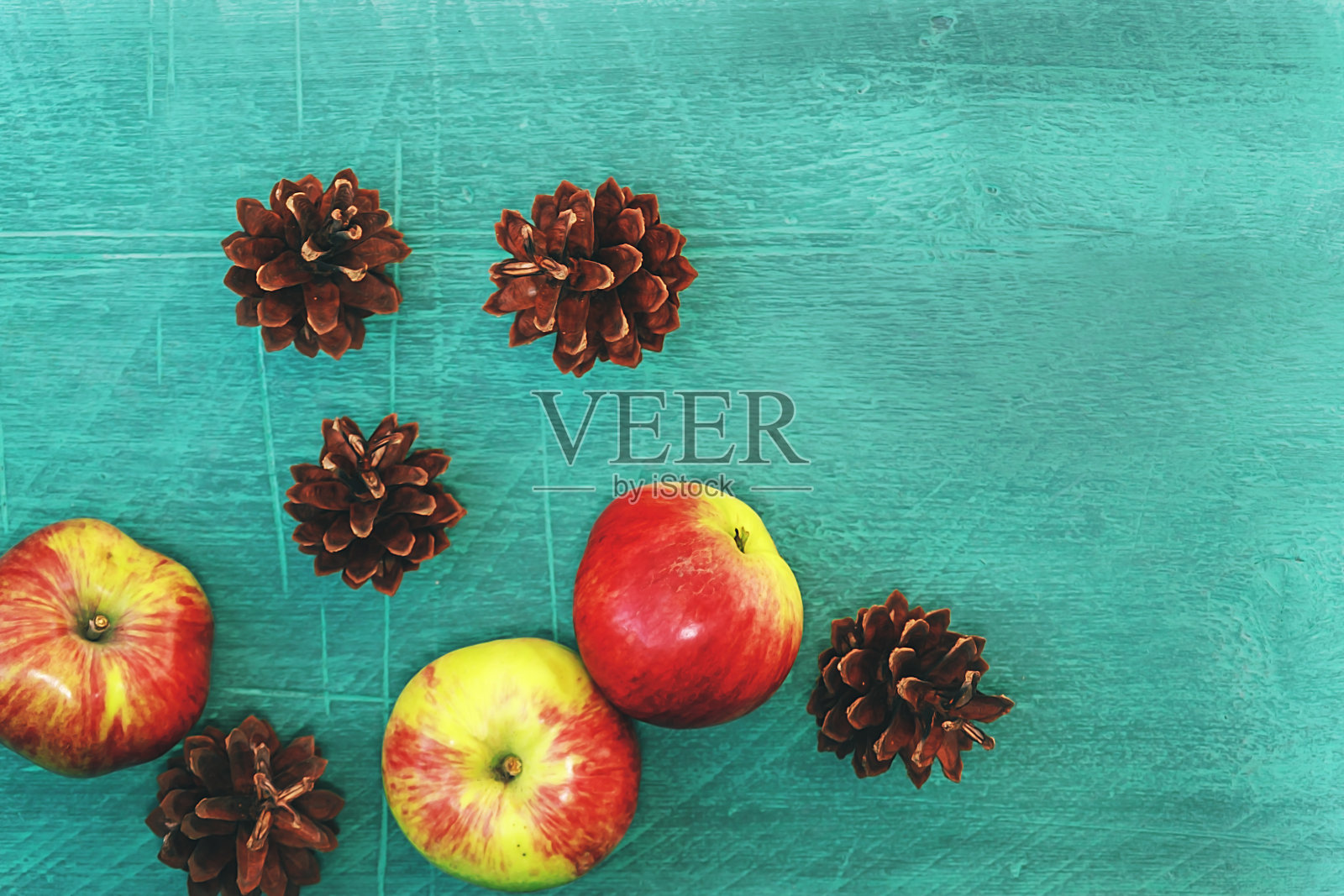 深绿色的背景与松果，红苹果在木桌上。可爱的颜色照片摄影图片