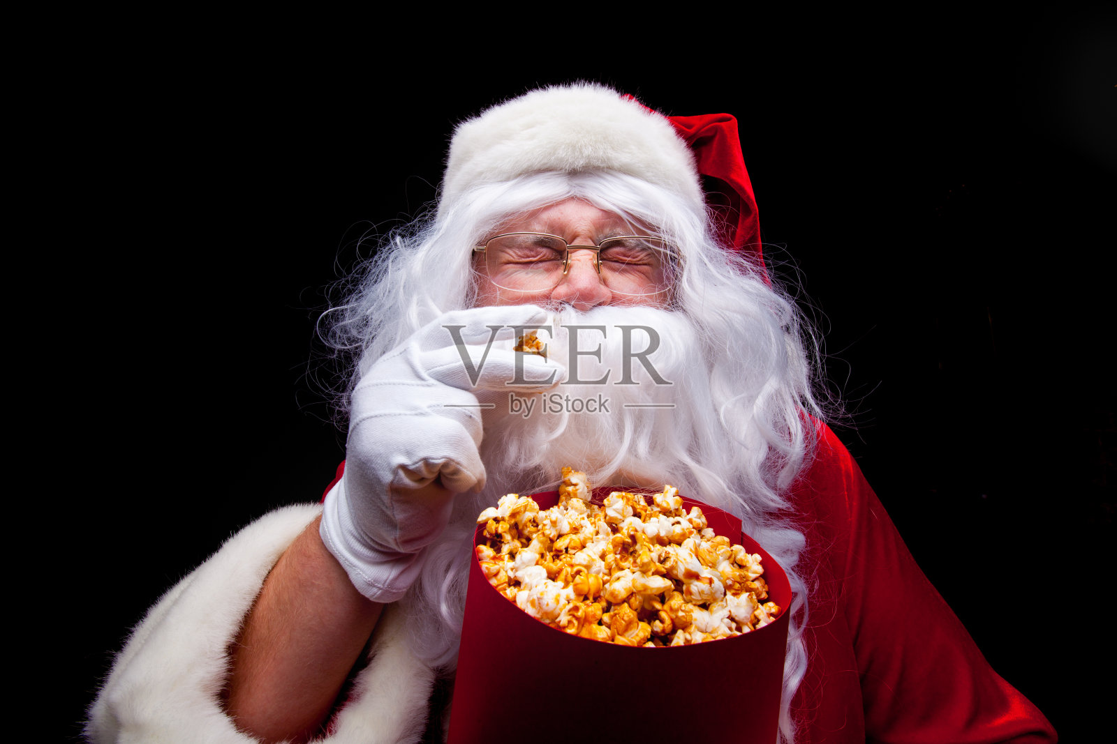 圣诞节。圣诞老人戴着手套的手与一个红桶爆米花，在一个黑色的背景照片摄影图片