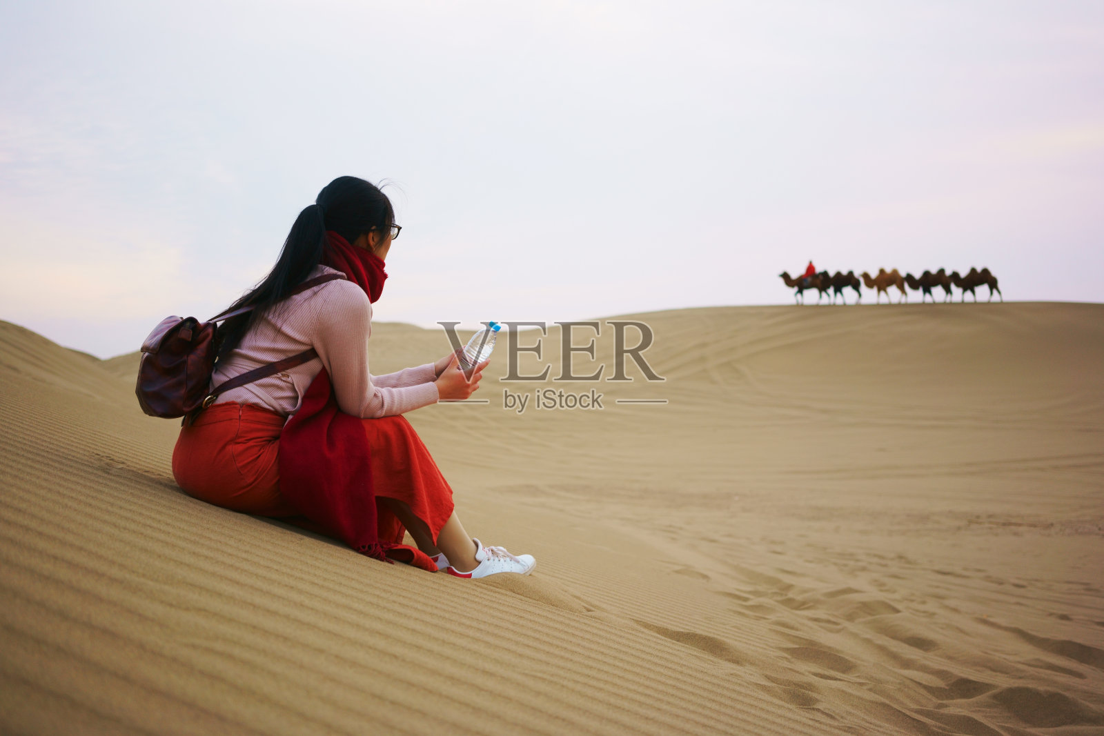 在沙漠日出时，女人在沙丘上放松照片摄影图片