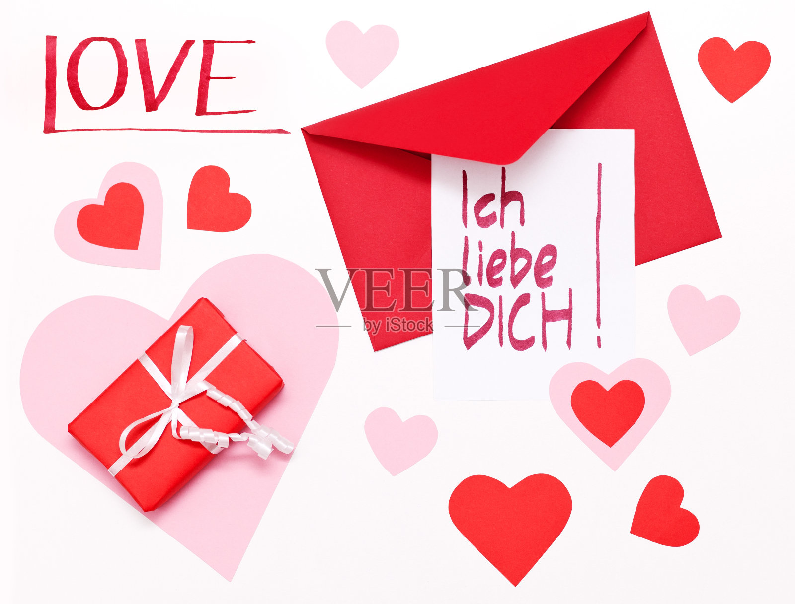 情人节的便条(德语)放在一个红信封上，旁边是一个红包裹。照片摄影图片